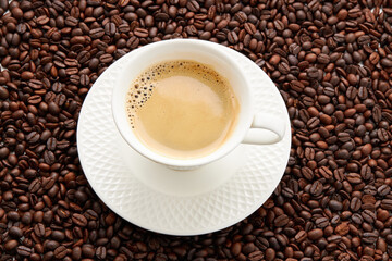 Wall Mural - Top view of coffee in white cup place on surface many roasted coffee beans background.