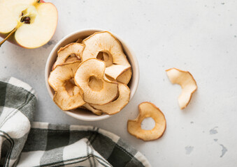 Wall Mural - Top view of bowl with dried apple rings on light background with ripe apple slice and kitchen towel.Macro.