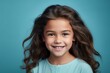 © Nerea - Close up portrait of a cute little girl with long curly hair smiling at camera on blue background