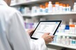 © olga_demina - pharmacist using a tablet to manage inventory against the backdrop of stocked pharmacy shelves