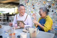 In The Pottery Workshop, An Asian Retired Couple Is Engaged In Pottery Making And Clay Painting Activities.