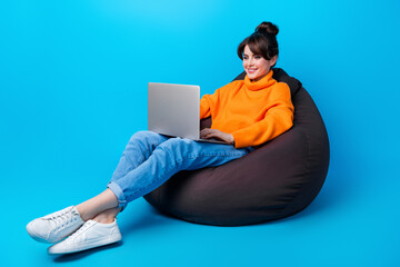 Wall Mural - Photo of positive pretty woman dressed orange sweater sitting bean bag working modern device isolated blue color background