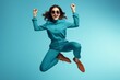 Full length photo of shiny lucky girl dressed brown shirt spectacles jumping high rising fists isolated blue color