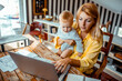 © Marko Geber - Mother holding baby using laptop at home