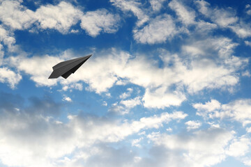 Wall Mural - Black paper plane flying in blue sky with clouds