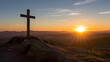 Christian cross on top of a hill facing the rays of a new dawn rising from the horizon. Symbolic of the resurrection of Jesus Christ, hope through faith, a new beginning.
