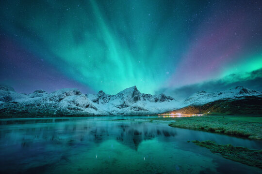northern lights over the snowy mountains, frozen sea, reflection in water at winter night in lofoten