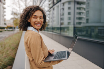 Wall Mural - Happy business woman working laptop while standing outside on background of office building