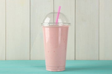 Wall Mural - Tasty smoothie in plastic cup on light blue table against white wooden wall