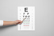Ophthalmologist pointing at vision test chart on gray background, closeup