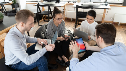 Wall Mural - Focused multiracial colleagues sit in circle in office work on modern gadgets during casual meeting. Concentrated diverse multiethnic employees busy with devices at briefing at workplace.