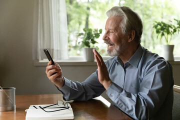 Wall Mural - Videocall. Happy grey haired aged man grandpa using phone to talk to grandchild online wave hand to webcam glad to say hello. Smiling mature male retiree calling friend in app for video conversations