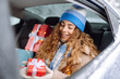 Young woman rides in the back seat of a car and holds a New Year's gift in her hands. Great winter day, festive mood.  In anticipation of the winter holidays, preparation and shopping concept.
