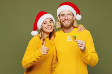 Canvas Print - Merry young couple two friends man woman wears sweater Santa hat posing use mobile cell phone credit bank card show like isolated on plain green background. Happy New Year Christmas holiday concept.