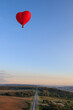 Heart shaped a hot air balloon flies with people over forests and fields in the morning at dawn