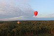 Two hot air balloons with people are flying over forests and fields in the morning at dawn