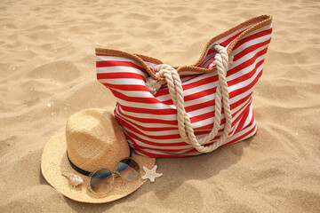 Wall Mural - Stylish striped bag with straw hat, sunglasses, seashell and starfish on sand. Beach accessories