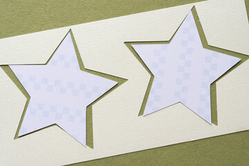 Poster - paper stencil with star cutouts and smaller paper stars with cube pattern on rough green paper