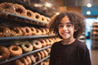 Young child with curly hair in front of brown donuts, smiling and curious, joyful exploration in a bakery or shop