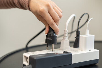 Closed up hand of woman plugged in, unplugged electricity cord cable on socket on table for energy saving, electric power on plate outlet, control expense electrical appliances, environment concept.