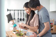 © DG PhotoStock - Happy cheerful Asian young couple preparing a vegetable salad in kitchen together in weekend.