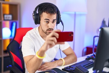 Sticker - Handsome hispanic man playing video games with smartphone scared and amazed with open mouth for surprise, disbelief face