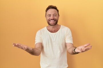 Sticker - Middle age man with beard standing over yellow background smiling cheerful with open arms as friendly welcome, positive and confident greetings