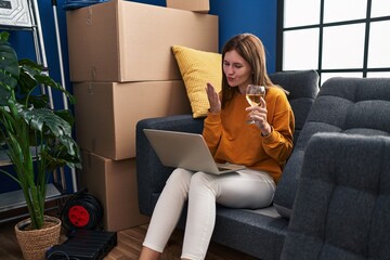 Canvas Print - Young blonde woman having video call drinking wine at new home