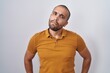 Hispanic man with beard standing over white background in shock face, looking skeptical and sarcastic, surprised with open mouth