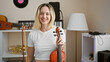 Young blonde woman musician holding violin smiling at music studio