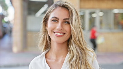 Wall Mural - Radiant young blonde woman, exuding confidence with a sparkling smile, stands outdoors on a sunny city street, enjoying the urban ambiance and spreading positive vibes.