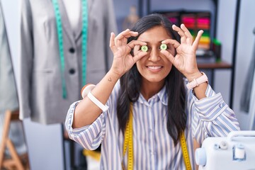 Sticker - Young beautiful hispanic woman tailor smiling confident holding buttons over eyes at clothing factory