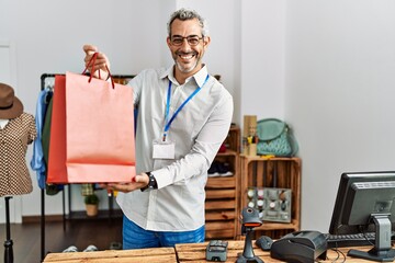 Wall Mural - Middle age grey-haired man shop assistant holding shopping bag at clothing store