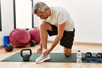 Wall Mural - Middle age grey-haired man tying shoe at sport center