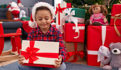 Canvas Print - Adorable hispanic boy unpacking gift sitting by christmas tree at home