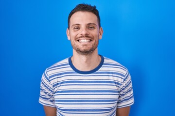 Wall Mural - Young hispanic man standing over blue background with a happy and cool smile on face. lucky person.