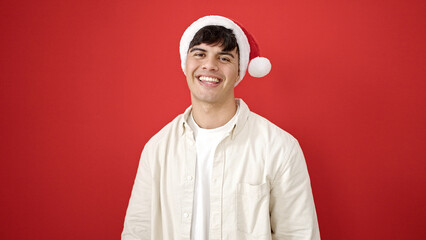 Sticker - Young hispanic man smiling confident wearing christmas hat over isolated red background