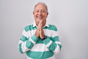 Wall Mural - Senior man with grey hair standing over white background praying with hands together asking for forgiveness smiling confident.