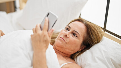 Poster - Middle age hispanic woman looking smartphone lying on bed at bedroom