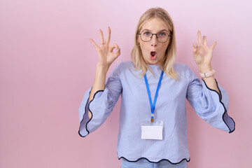 Poster - Young caucasian business woman wearing id card looking surprised and shocked doing ok approval symbol with fingers. crazy expression