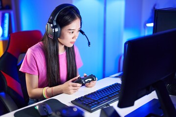 Sticker - Young chinese woman streamer playing video game using joystick at gaming room