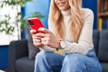 Sticker - Young blonde woman using smartphone sitting on sofa at home