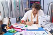 © Krakenimages.com - Young hispanic man tailor smiling confident drawing on notebook at clothing factory