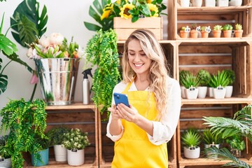 Wall Mural - Young blonde woman florist smiling confident using smartphone at florist