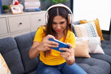 Poster - Young beautiful arab woman playing video game sitting on sofa at home