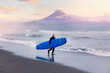 Surfer with surfboard on black sand on background volcano Kamchatka, winter surfing in ocean