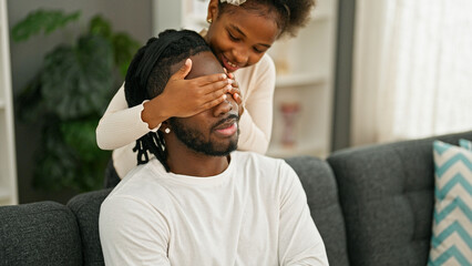 Wall Mural - African american father and daughter sitting on sofa surprise covering eyes with hands at home