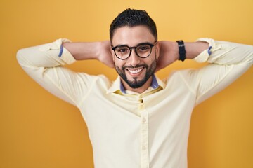 Wall Mural - Hispanic young man wearing business clothes and glasses relaxing and stretching, arms and hands behind head and neck smiling happy