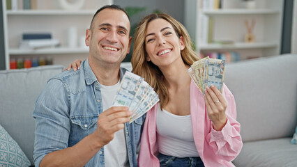 Man and woman couple hugging each other holding peruvian soles banknotes at home