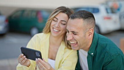 Poster - Man and woman couple sitting on bench watching video on smartphone at street